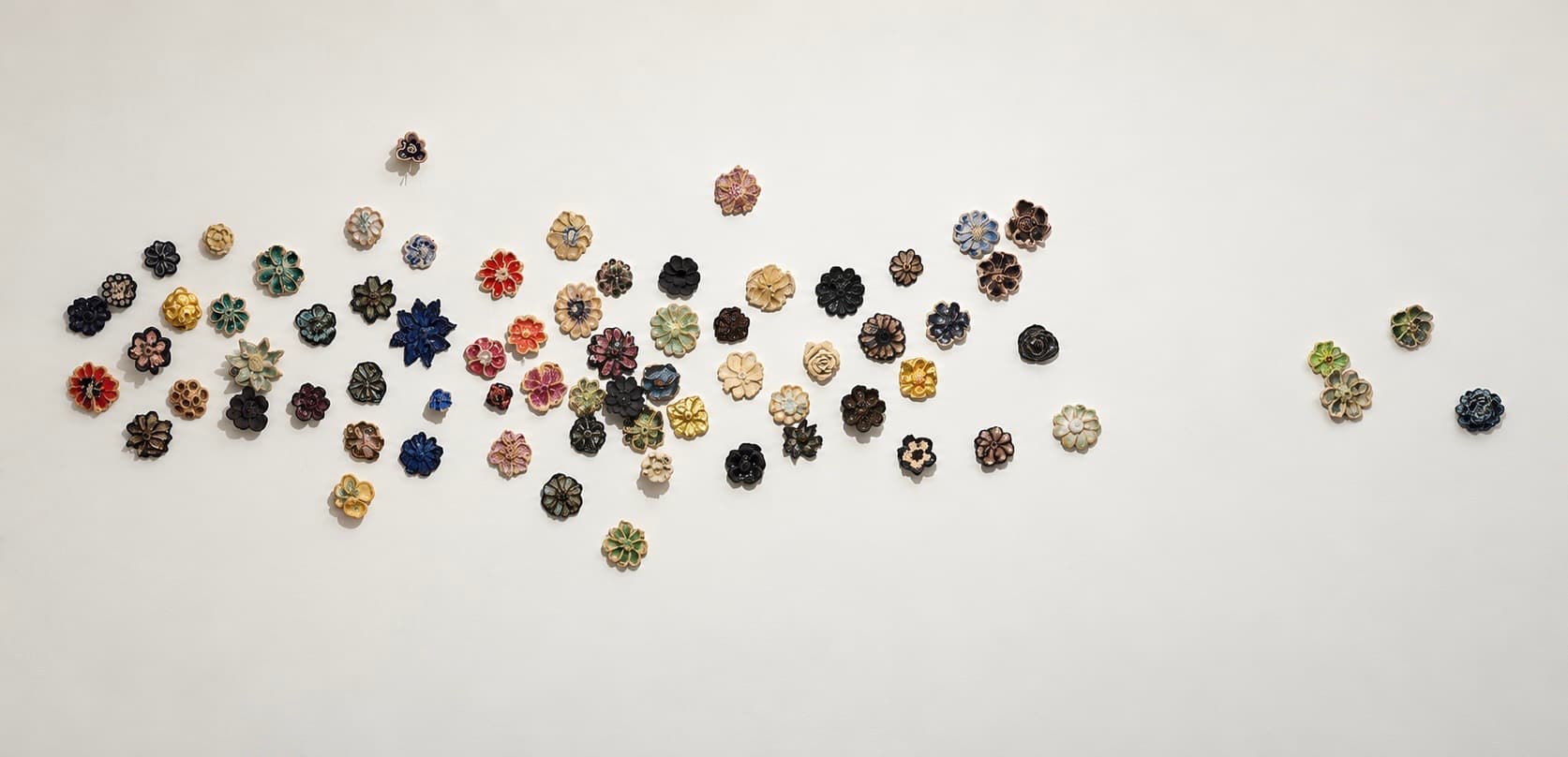 Glazed ceramic flower fragments scattered across a white wall